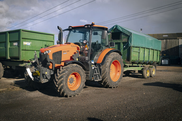 Orange tractor with a green trailer in a farmyard.
